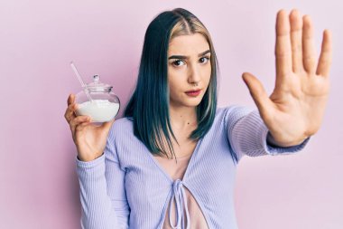 Genç modern bir kız elinde şekerli bir kaseyle dur işareti yapıyor ciddi ve kendinden emin bir ifadeyle savunma hareketi yapıyor. 