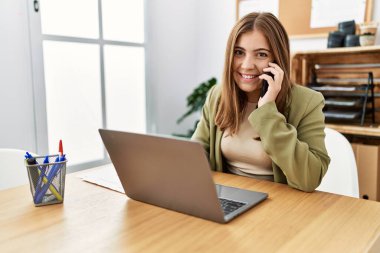 Ofiste çalışan, akıllı telefondan konuşan genç İspanyol kadın.