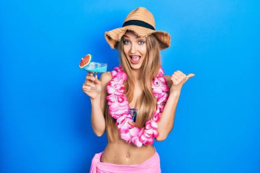 Bikini giyen genç sarışın kız ve Hawaii zambağı içen kokteyl içen parmak uçlarını yana doğru gösteren mutlu bir ağızla gülümseyen kız. 