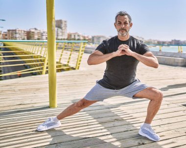 Orta yaşlı İspanyol adam deniz kenarında esneme hareketleri yapıyor.