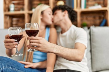 Genç çift evde kırmızı şarap kadehiyle öpüşüp kadeh kaldırıyor..