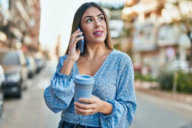 Genç İspanyol kadın akıllı telefondan konuşuyor ve şehirde kahve içiyor.