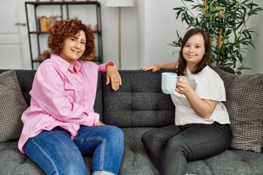 Olgun anne ve Down sendromlu kız evde, kanepede oturmuş sohbet ediyorlar.