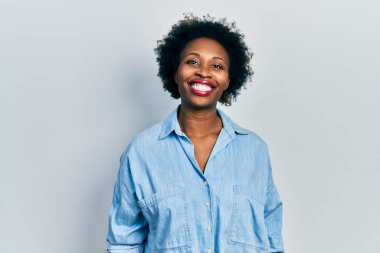 Genç Afro-Amerikalı kadın günlük kıyafetler giyiyor. Pozitif ve mutlu görünüyor. Kendine güvenen bir gülümsemeyle dişlerini gösteriyor. 