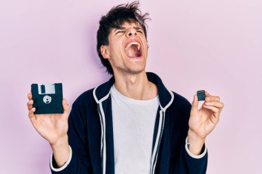 Yakışıklı hippi genç adam disket ve SDxc kartı tutuyor kızgın ve kızgın bağırıyor hayal kırıklığına uğramış ve öfkeli, öfkeyle bağırıyor. 