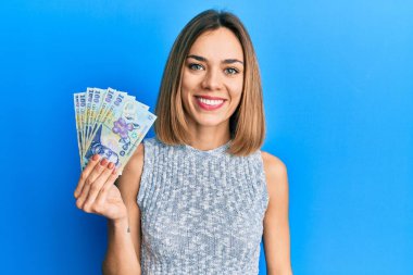 Genç, beyaz, sarışın bir kadın elinde 100 Romen leyi banknotları tutuyor. Pozitif ve mutlu görünüyor. Kendine güvenen bir gülümsemeyle dişlerini gösteriyor. 