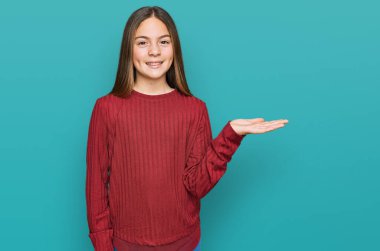 Güzel, esmer, sıradan bir kazak giymiş neşeli bir şekilde gülümseyen ve avuç içi kameraya bakan küçük bir kız.. 