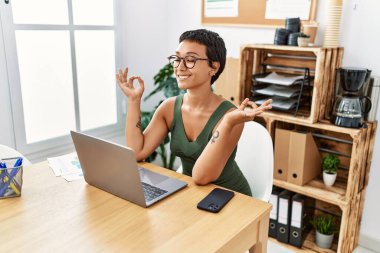 Ofiste yoga yaparken kendine gülen genç İspanyol kadın.