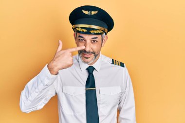 Yakışıklı, orta yaşlı, gri saçlı, uçak pilotu üniforması giyen, el parmağı ve burnu olan, neşeli gülümseyen biri. güzellik konsepti 