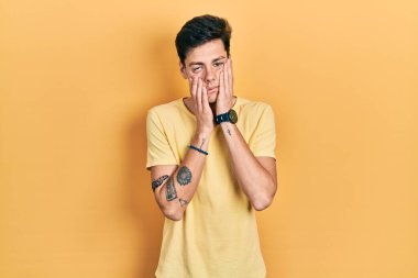 Günlük sarı tişört giyen genç İspanyol adam yorgun eller yüzünü kapatıyor, depresyon ve üzüntü, sorun için üzgün ve rahatsız 
