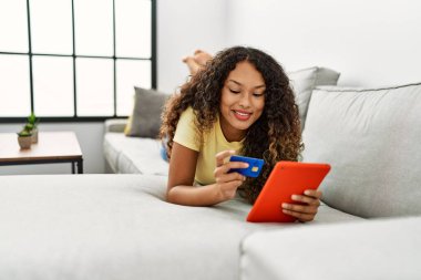 Evde dokunmatik ped ve kredi kartı kullanan kendine güvenen genç Latin bir kadın.