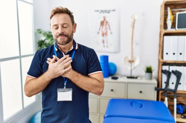 Orta yaşlı fizyoterapist. Ağrı giderme kliniğinde çalışıyor. Elleri göğsünde, gözleri kapalı ve yüzünde minnettarlıkla gülümsüyor. sağlık kavramı. 