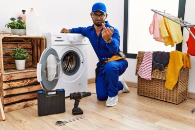 Young indian technician working on washing machine showing middle finger, impolite and rude fuck off expression 