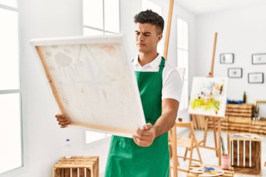 Young hispanic man looking draw canvas at art studio