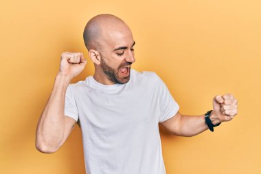 Genç kel adam, günlük beyaz tişört giyiyor mutlu ve neşeli dans ediyor, gülümsüyor rahat ve kendinden emin bir şekilde müzik dinliyor. 