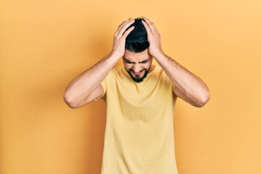 Sakallı, sıradan sarı tişörtlü, baş ağrısı çeken, çaresiz ve stresli yakışıklı bir adam. Çünkü acı ve migren ağrısı var. Eller başının üstünde.. 