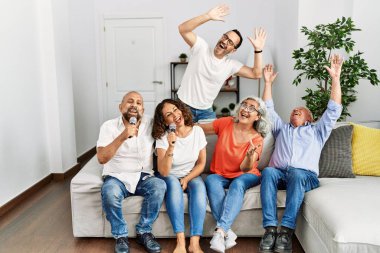 Bir grup orta yaşlı arkadaş evde mikrofon kullanarak şarkı söylüyor..