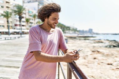 Genç İspanyol adam kumsalda dururken mutlu bir şekilde gülümsüyor..