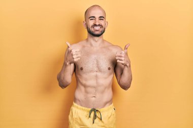 Mayo giyen genç kel bir adam elinde olumlu jest yapıyor, gülümsüyor ve mutlu. Neşeli ifade ve kazanan jest. 