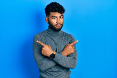 Balıkçı yaka kazak giyen sakallı bir Arap her iki tarafı da parmaklarıyla işaret ediyor. Farklı yönlere. 