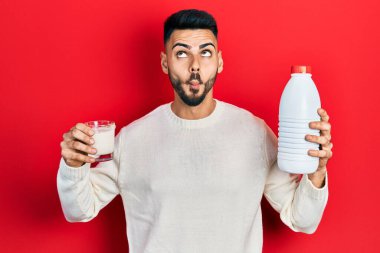 Sakallı, elinde bir bardak süt ve plastik şişeyle genç İspanyol bir adam. Ağzı ve şaşı gözleriyle balık suratı yapıyor. Deli ve komik.. 