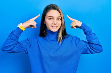 Balıkçı yaka kazak giyen genç esmer kız iki eliyle başını gösteren gülümseme, harika bir fikir ya da düşünce, iyi bir hafıza 