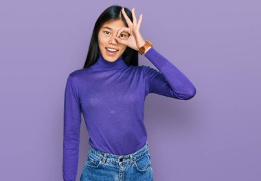 Güzel, genç Asyalı bir kadın günlük kıyafetler giyiyor. El hareketleriyle gülümsüyor ve mutlu yüzüyle parmaklarının arasından bakıyor.. 