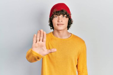 Handsome young man wearing wool hat doing stop sing with palm of the hand. warning expression with negative and serious gesture on the face. 