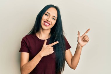 Gündelik tişört giyen genç İspanyol kız gülümseyip kameraya bakıyor ve iki eliyle ve parmaklarıyla kenarı işaret ediyor.. 