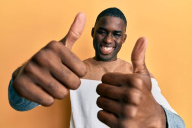 Genç Afro-Amerikan adam günlük giysiler giyip olumlu jestler yapıyor. Elleriyle gülümsüyor ve başarı için seviniyor. kazanan jest. 