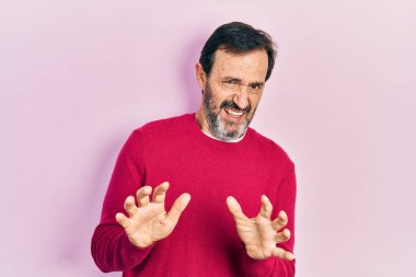 Orta yaşlı İspanyol bir adam günlük giysiler giyer, tiksinti ifadesi takınır, tiksinti ifadesi takınır ve tiksinti ifadesi takınır. Eller havada. 