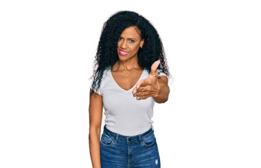 Orta yaşlı Afro-Amerikalı kadın, günlük beyaz tişört giyip dostça gülümseyerek selamlaşma ve selamlama sunuyor. başarılı iş. 