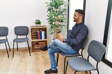 Genç İspanyol adam bekleme odasında sandalyeye oturmuş kahve içiyor.