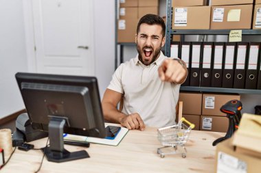 Handsome hispanic man working at small business commerce pointing displeased and frustrated to the camera, angry and furious with you 