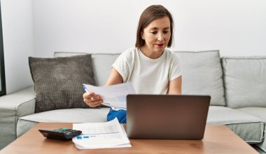 Orta yaşlı İspanyol kadın ev işlerinde ev işleri için dizüstü bilgisayar kullanıyor.