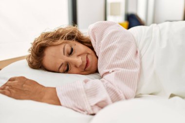 Orta yaşlı beyaz kadın yatak odasında yatakta yatıyor..