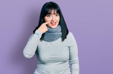 Latin kökenli genç ve uzun boylu bir kadın. Kış eşarbı takıyor. Parmak omuza ve burun buruna, neşeyle gülümsüyor. güzellik konsepti 