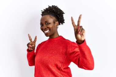 Genç Afrikalı Amerikalı kadın izole edilmiş arka planda günlük giysiler giyip parmaklarını zafer işareti yaparken gösteren kameraya gülümsüyor. İki numara.. 