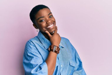 Genç Afro-Amerikan kadın günlük kıyafetler giyiyor kameraya bakıyor kollarını kavuşturup gülümsüyor ve çenesini kaldırıyor. Olumlu düşünmek. 