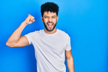 Sakallı, sıradan beyaz tişörtlü, sinirli, kızgın, sinirli ve öfkeliyken öfkeyle bağıran genç bir Arap. öfke ve agresif konsept. 