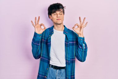 Yakışıklı hippi genç adam gündelik beyaz tişört ve klasik gömlek giyer rahatlar ve gözleri kapalı gülümser parmaklarıyla meditasyon jesti yapar. yoga konsepti. 