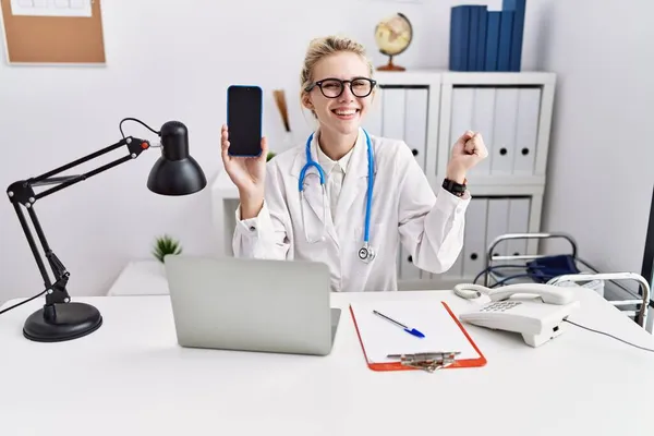 スマートフォンを持っている若い医師の女性は誇りに思って叫んで空白の画面を示しています 勝利と成功を祝います非常に腕を上げ興奮 — ストック写真