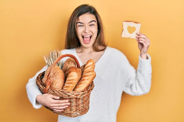 年轻的高加索女孩拿着装有面包的柳条篮和心形的面包庆祝胜利 她睁开眼睛尖叫着兴奋地惊叹成功 — 图库照片