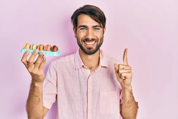 Young Hispanic Man Holding Delicious Macrons Pastries Smiling Idea Question — Stock Photo, Image