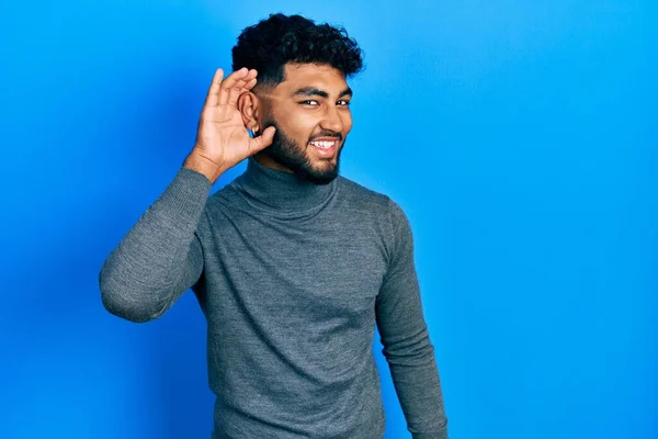 噂やゴシップに耳を傾ける耳の上に手で笑みを浮かべて亀のセーターを着てひげを持つアラブ人の男 聴覚障害の概念 — ストック写真