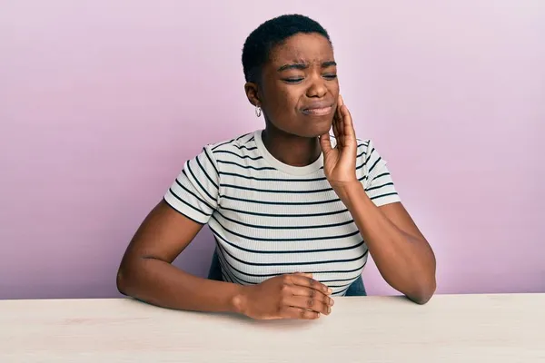 Młoda Afroamerykanka Ubrana Luźne Ubrania Siedząca Stole Dotykająca Ust Ręką — Zdjęcie stockowe