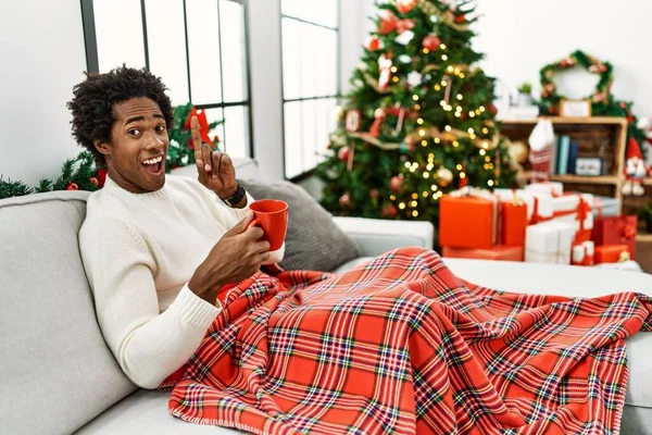 Joven Afroamericano Sentado Sofá Bebiendo Café Junto Árbol Navidad Señalando — Foto de Stock