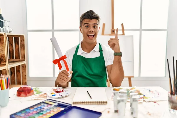 Young Hispanic Man Art Studio Holding Degree Pointing Finger Successful — стоковое фото