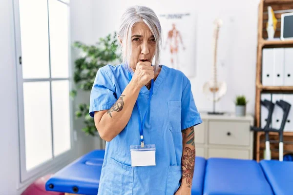 Medelålders Gråhårig Kvinna Bär Sjukgymnast Uniform Läkarmottagningen Sjukdomskänsla Och Hosta — Stockfoto