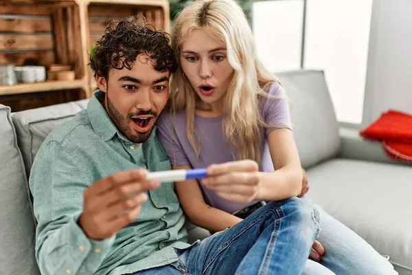 年轻夫妇惊讶地看着家里的怀孕测试结果 — 图库照片